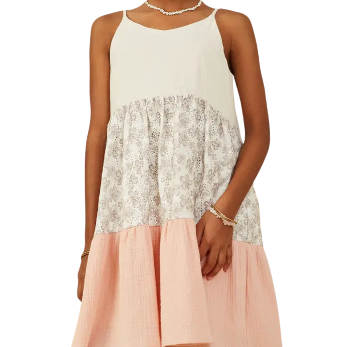 Tween girl wearing a sleeveless color block dress with cream bodice, floral print tier, and peach textured skirt.