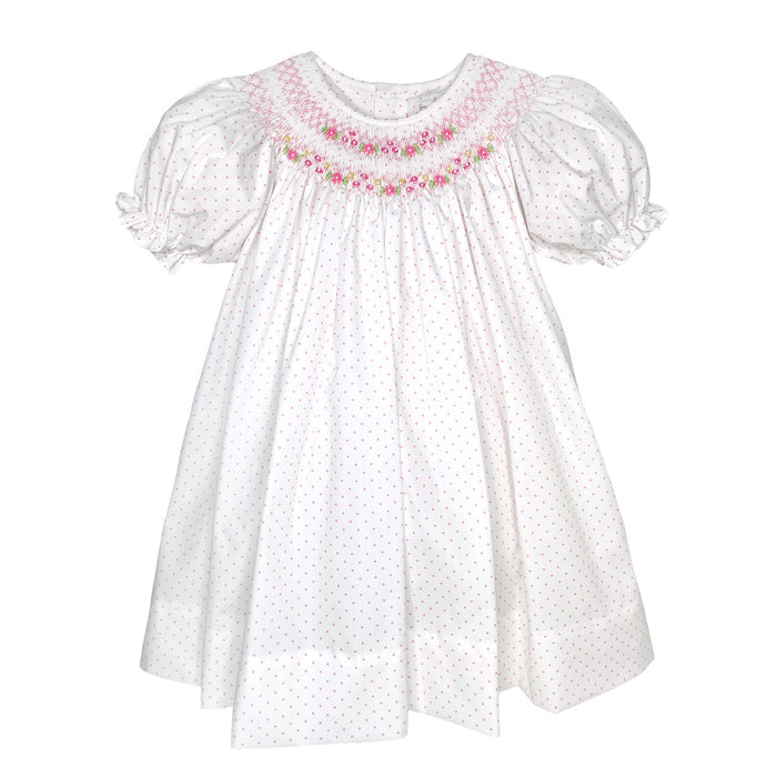 White girls smocked dress with pink polka dots, floral hand smocking at neckline, and puff sleeves on a plain white background.