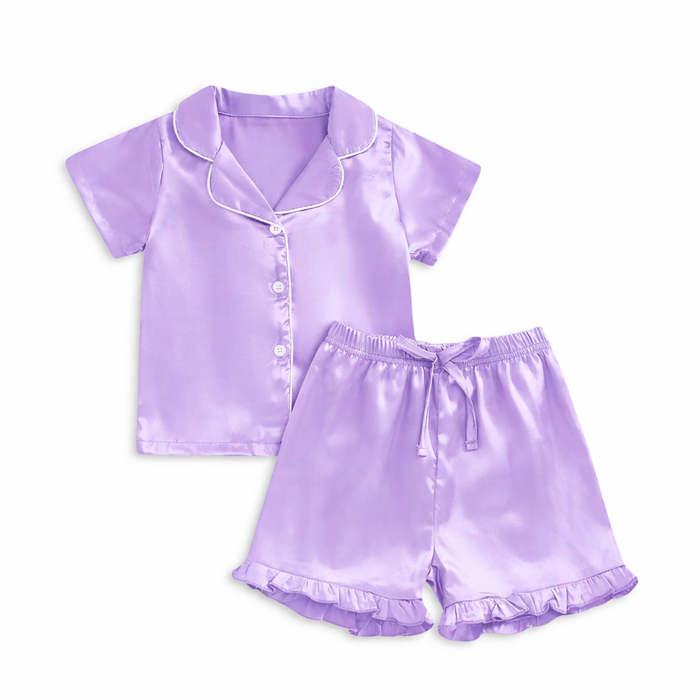 Lavender satin girls pajama set with short-sleeve button-up top, white piping detail, and ruffle hem shorts on white background.