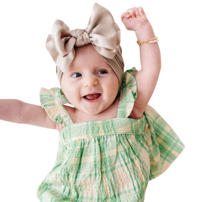 Baby wearing a champagne satin knot headband with a green plaid outfit