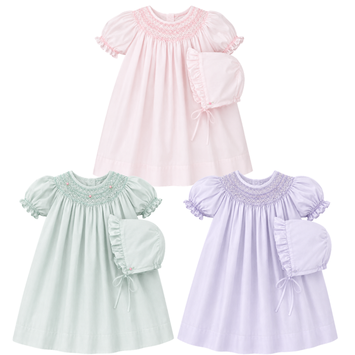 Three baby dresses in pink, mint, and purple with smocked details on a white background.