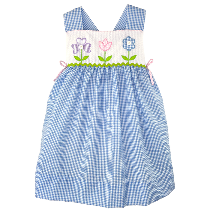 Girls blue seersucker dress with floral appliqué bodice, wide shoulder straps, and side bow accents on white background.
