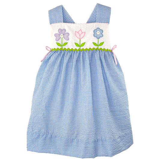 Girls blue seersucker dress with floral appliqué bodice, wide shoulder straps, and side bow accents on white background.