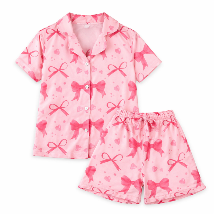 Girls pink pajama set with bow and heart print, short-sleeve button-up top and matching shorts on white background.