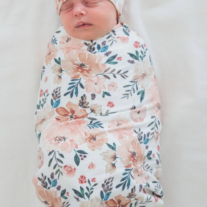 Newborn baby swaddled in a floral copper pearl blanket on a white background