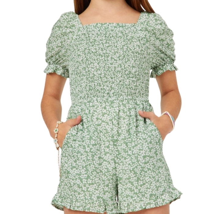 Tween girl wearing a sage green floral romper with smocked bodice, puff sleeves, and ruffle hem.