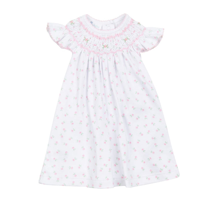 White baby bishop dress with pink floral print, hand-smocked neckline, flutter sleeves, and flowing silhouette on a white background