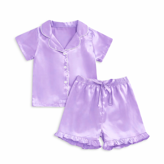 Lavender satin girls pajama set with short-sleeve button-up top, white piping detail, and ruffle hem shorts on white background.